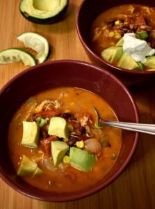 black bean and chicken soup in red bowls with avocado and limes