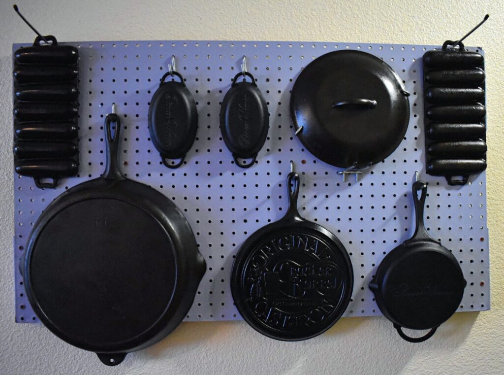 cast iron skillets, tops, molds, and dishes hanging on a periwinkle peg board