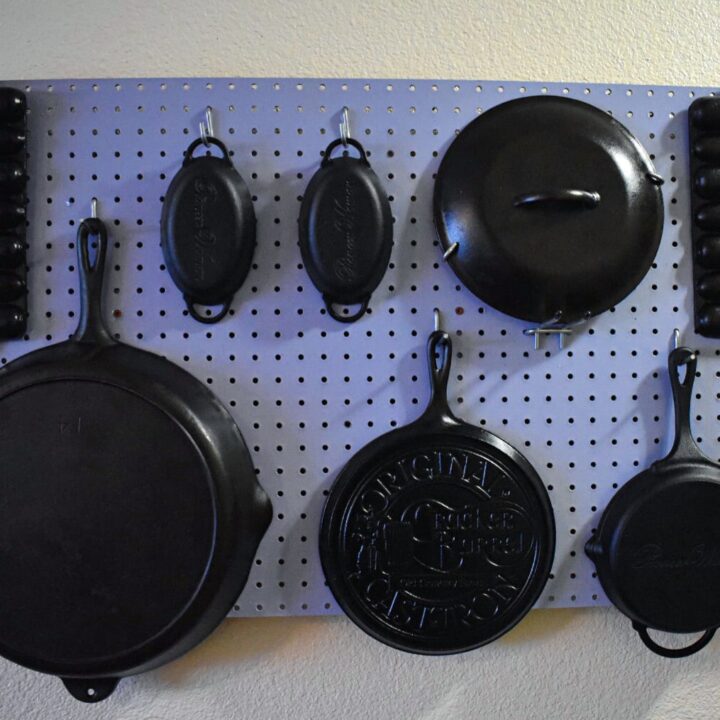 cast iron skillets, tops, molds, and dishes hanging on a periwinkle peg board