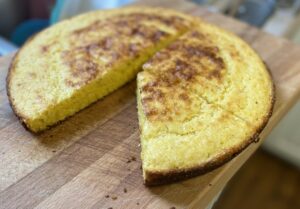 cast iron skillet corn bread with a slice taken out resting on wooden cutting board