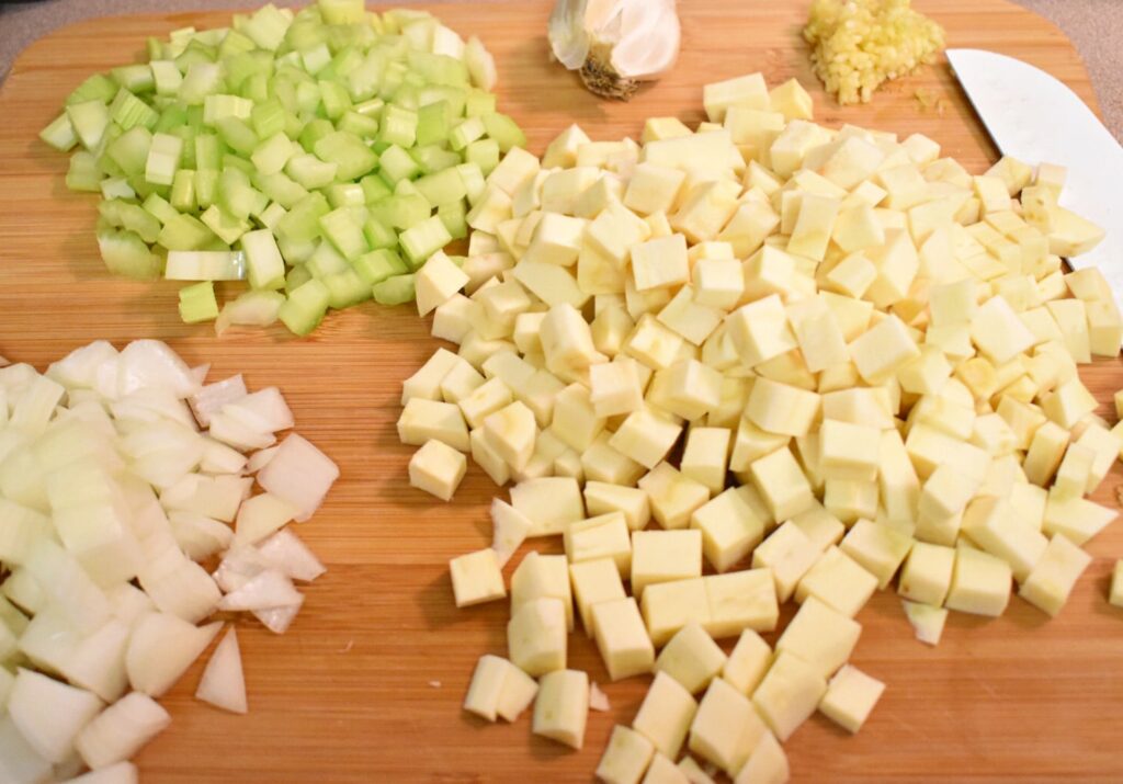 diced parsnips, celery, onions, and garlic on a wooden cutting board