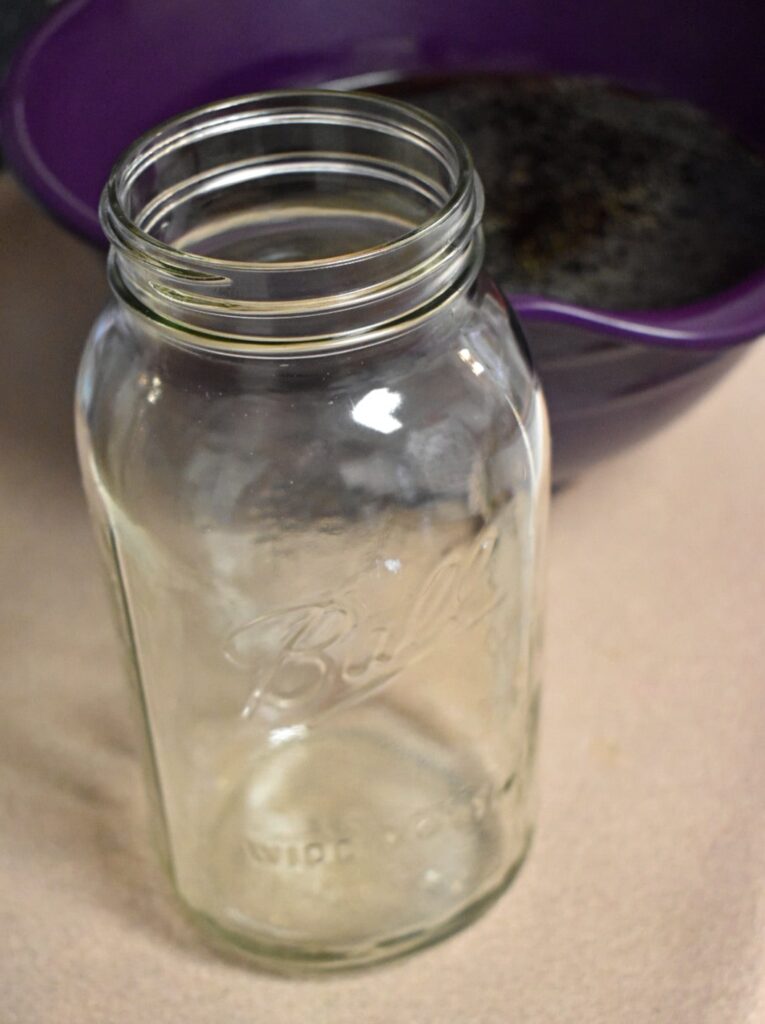 empty half gallon mason jar with a purple bowl of broth behind it