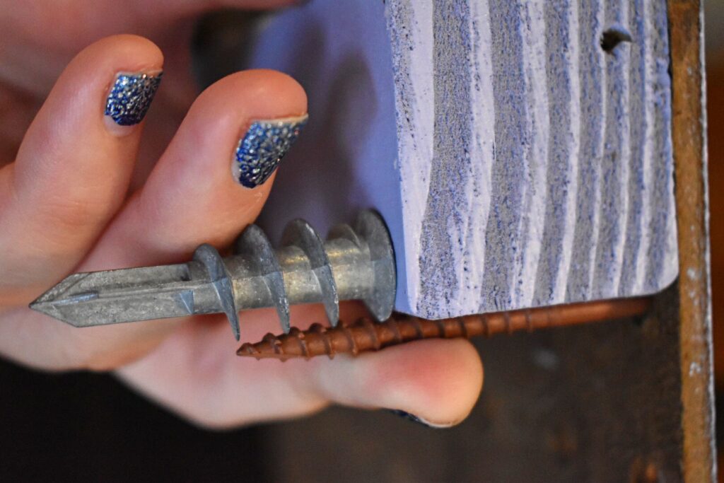 a screw, sheet rock anchor, and piece of wood comparing length and fit