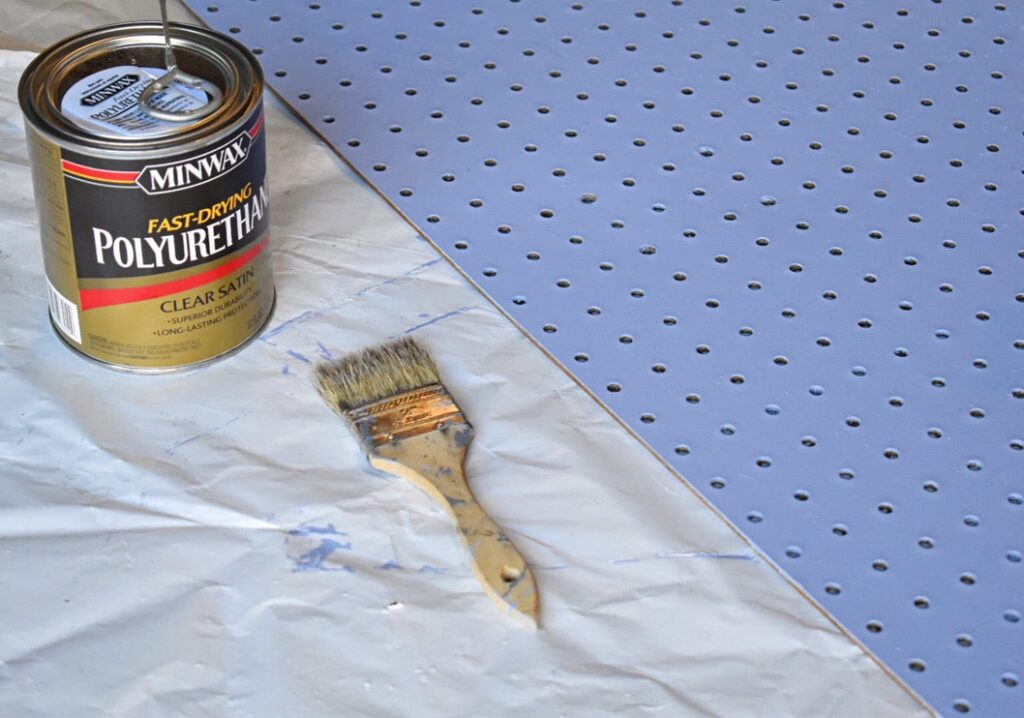 can of polyurethane, and a paint brush next to a painted periwinkle peg board