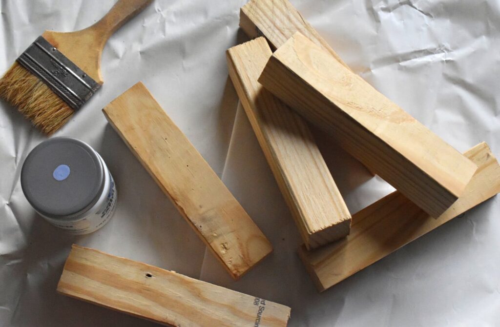 a stack of small pieces of wood, a paint brush, and a sample container of paint