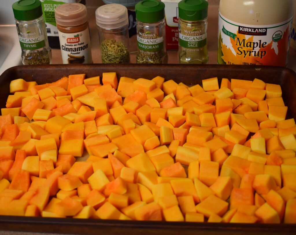 diced butternut squash on baking tray with maple syrup and seasonings behind it