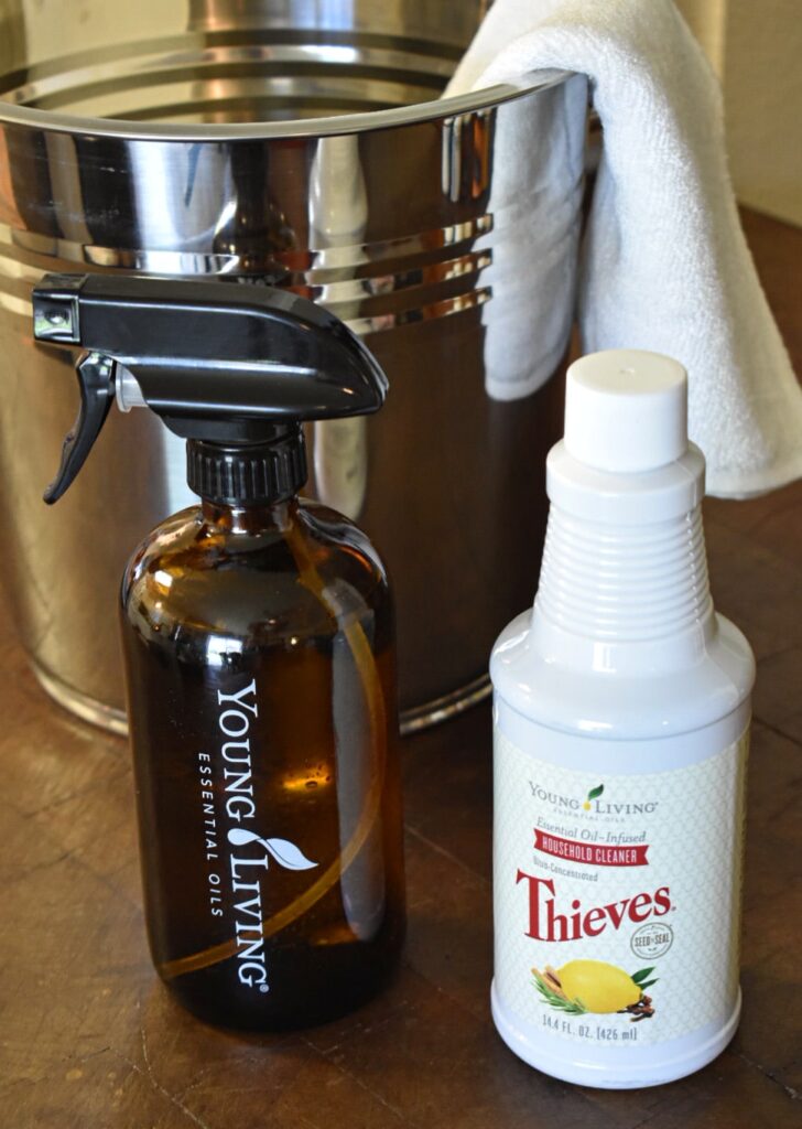 a glass young living spray bottle, thieves cleaner, a metal bucket, and a clean white rag