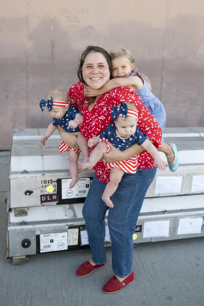 Sophia white a brunette woman carrying twin baby girls with a girl toddler on her back